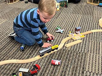 Young boy playing with toy trains on the floor. 