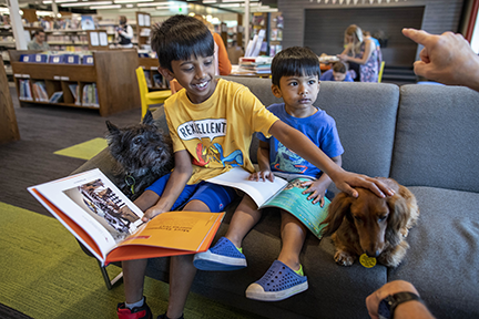 Two boys holding books and smiling with two dogs next to them.