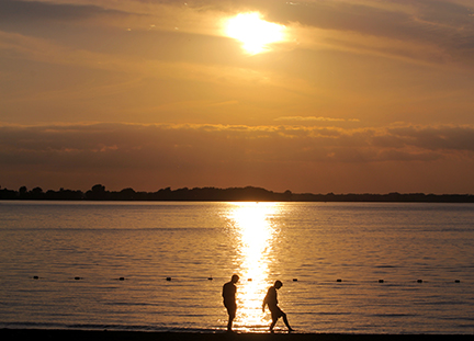Silhouette of two people walking on beach at sunset.