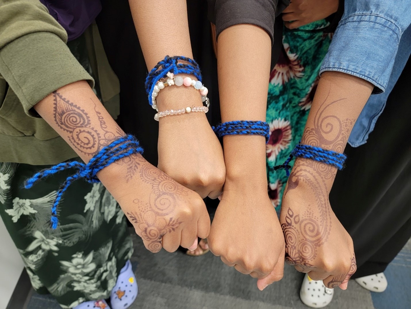 Closeup for four arms showing homemade bracelets and henna art.