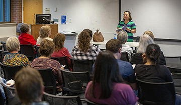 Group sitting in chairs, listening to a presenter at the front of the room.