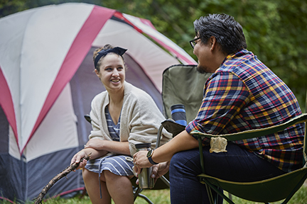 Two people sitting in camp chairs with tent in the background.