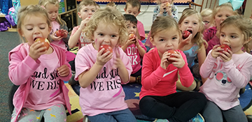 Children eating apples while sitting on the floor.