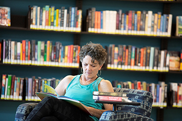 Woman reading in a lounge chair. Shelves of books behind her.