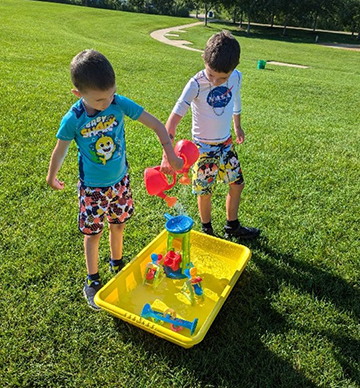 Kids playing with watering cans outside a library.