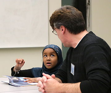 Volunteer tutor helping small child with reading a book.