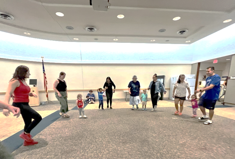 Group of kids and caregivers dancing at a library program.