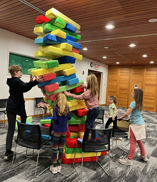 Five kids holding up a large block tower.