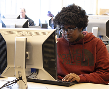 Teen boy sitting at a computer, looking at the monitor.