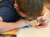 Teen boy drawing with markers on a piece of paper.