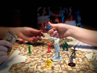 Closeup of Dungeons and Dragons board with two hands exchanging a multi-sided die..