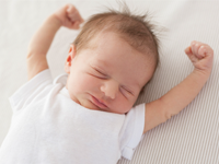 Baby with his eyes closed, stretching his arms out.