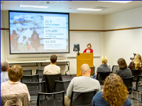 Woman presenting at a podium in front of a large group.
