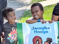 Two boys standing behind a book page posted in a park.