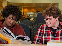 Two teen boys looking at a book together and smiling. 