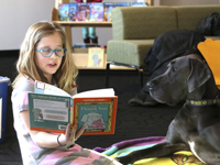 A girl reading to a therapy dog at a Waggin' Tales event.