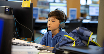 Boy with headphones sitting at a computer.