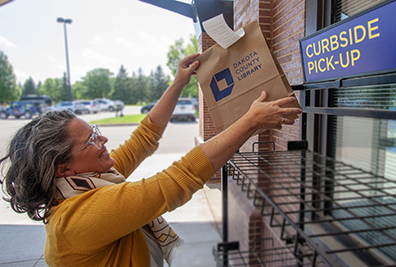 Woman grabbing a library bag from the curbside pick-up area.