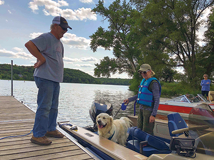 Woman in a boat with a dog. Main standing on the dock next to the boat.