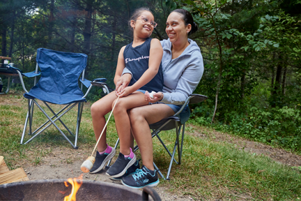 Mother and daughter sitting in camp chair roasting a marshmellows.