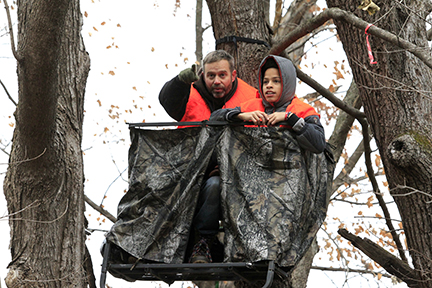 Two people in a deer stand. One is pointing into the distance.