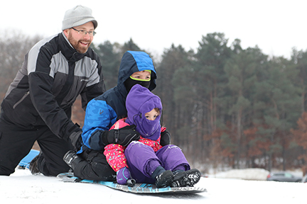 A father pushing two children on a sled down a hill.