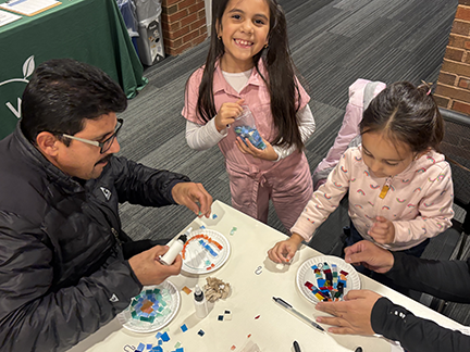 A father and two girls completing a mosaic art project.