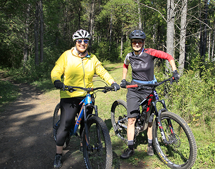 Two women smiling while on mountain bikes.