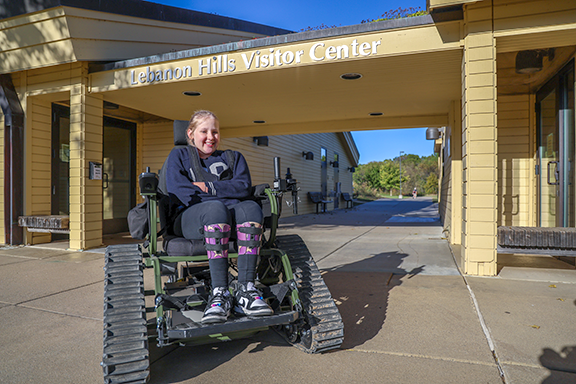 Girl sitting in a track chair in front of Lebanon Hills Visitor Center.
