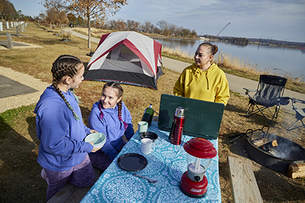 Family eating at a picnic table with tent in the background.