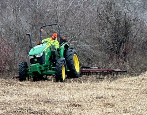 Man driving a tractor, power raking the area.
