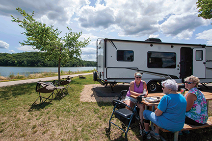 Three women sitting at a picnic table in front of an RV.