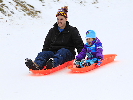 Man and child sledding at Whitetail Woods Regional Park.