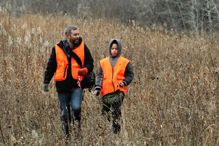 Father and son walking through tall grasses during a deer hunt.