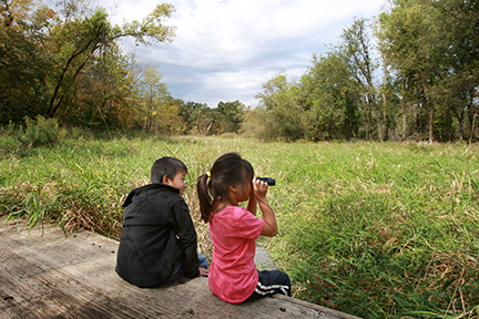 Two children sitting on a bench, using binoculars.